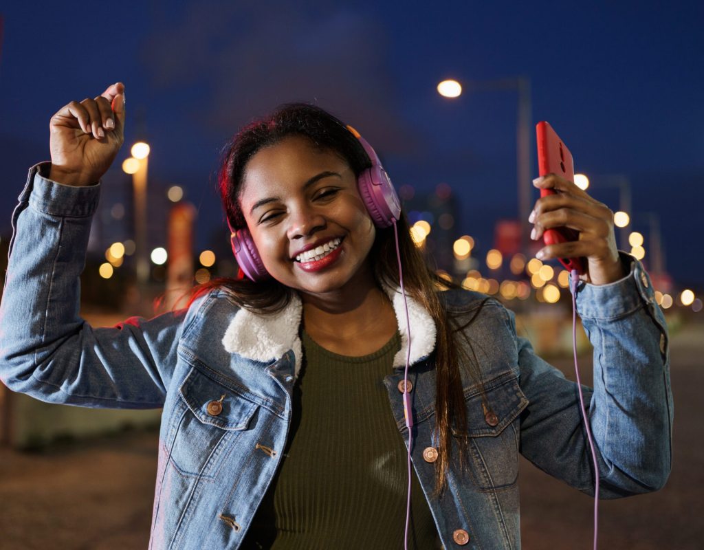 Young African American Latin Woman listening to salsa music on headphones and smartphone in the city at night